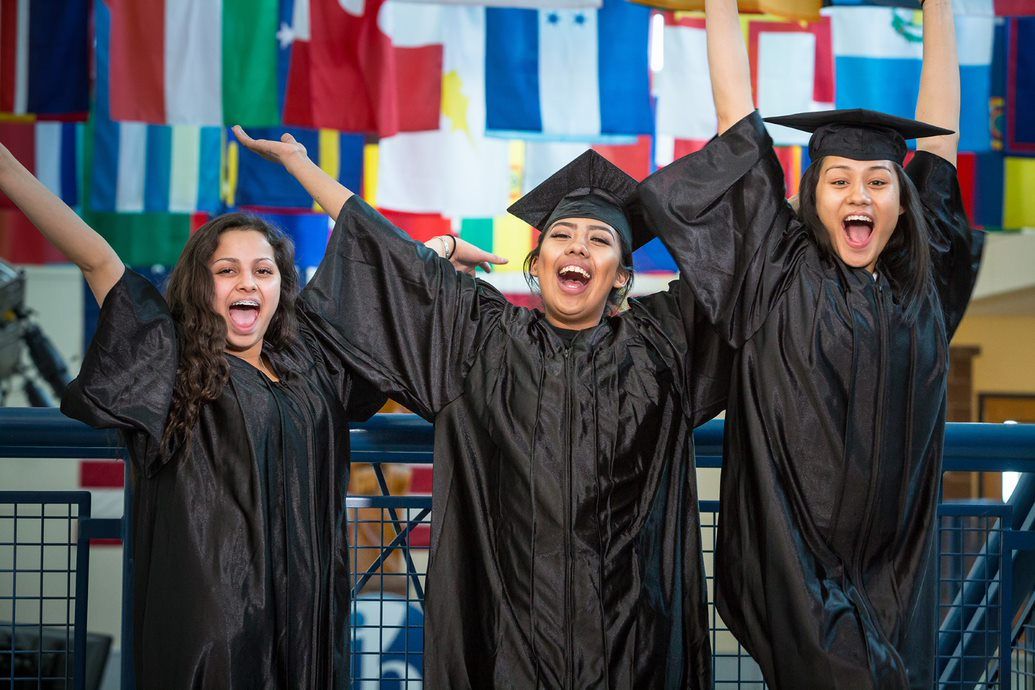 Three Female Students In Graduation Outfits Cheer