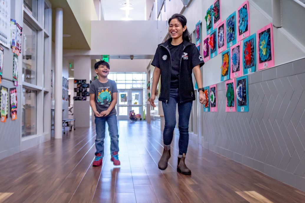 Female Teacher Walks With Her Grade-school Age Student Down The Hall