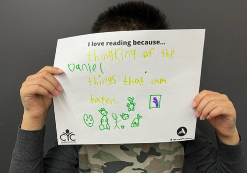Daniel holding up his "I love reading because..." drawing stating that he loves thinking of the things that can happen.